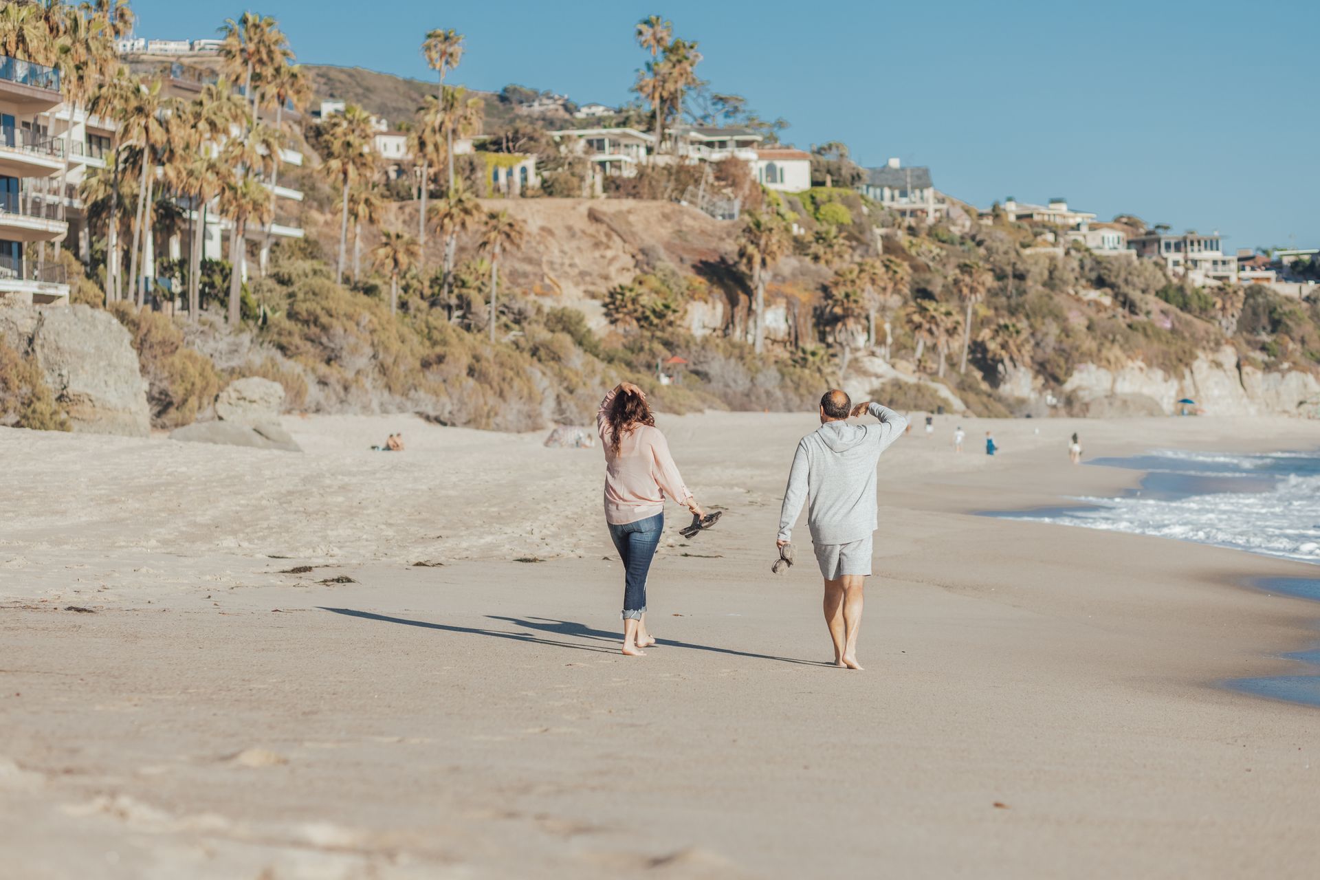 A couple walking along the shoreline of a sunny Southern California beach